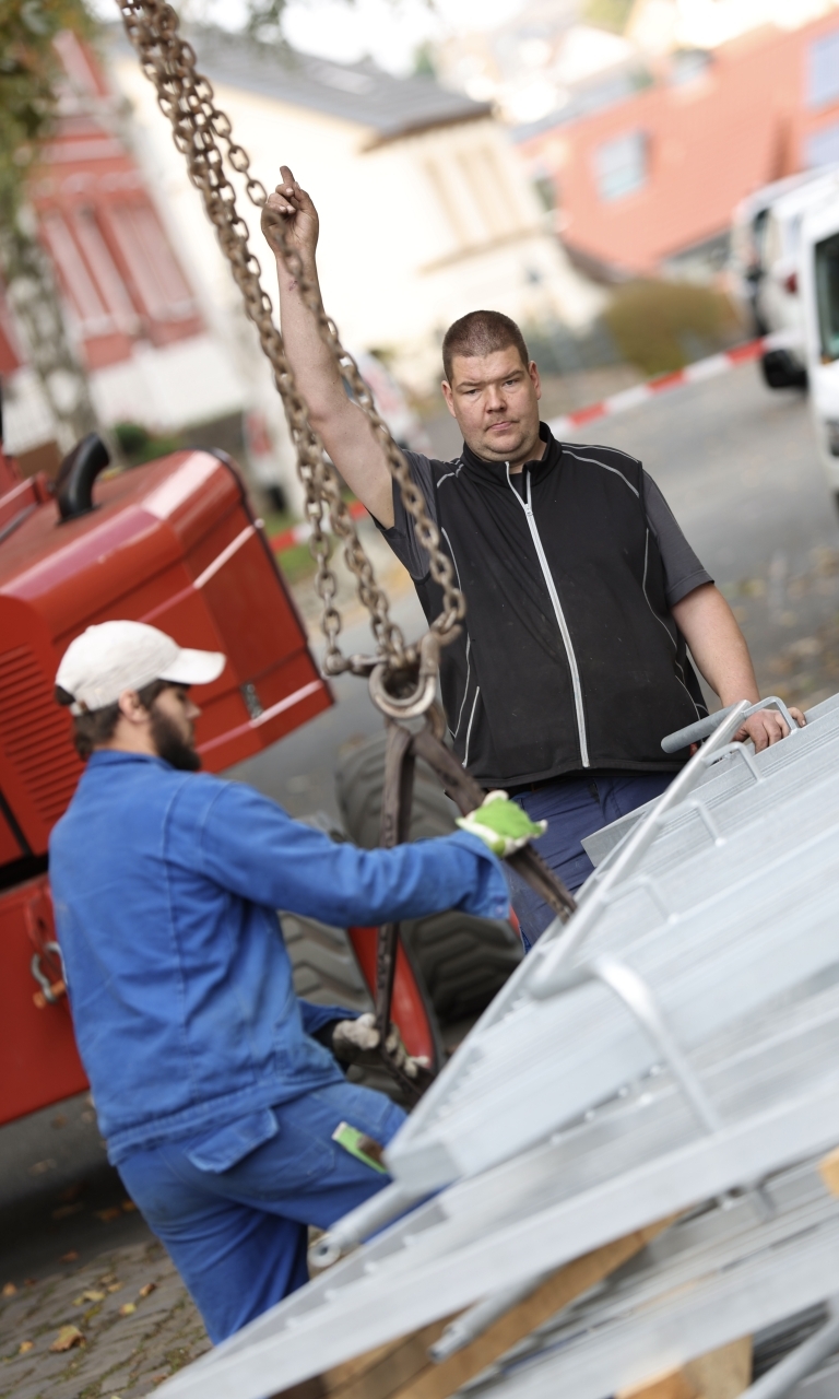 Zwei Männer in Arbeitsmontur stehen an einem Arbeitsgerät. 