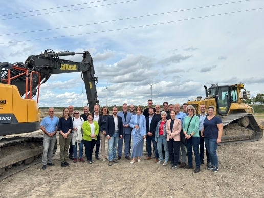 Vor einem Bagger und einer Raupe auf der Baustelle Im Dicken Dören steht eine Gruppe von Menschen.