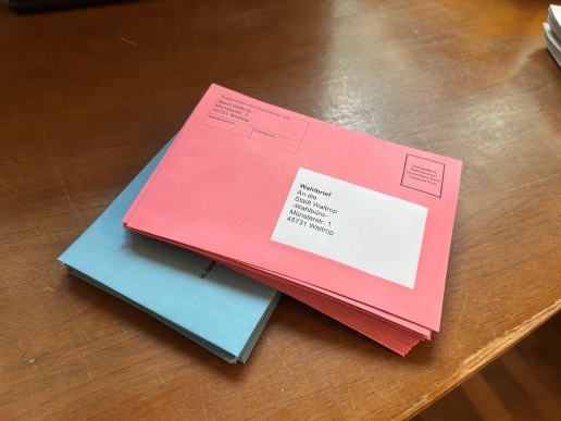 Ein Stapel Wahlbriefe in roten Umschlägen liegt auf einem Tisch.