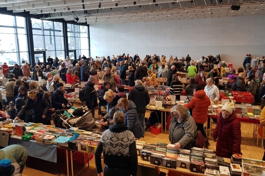 Beim Büchermarkt in der Stadthalle Waltrop stöbern viele Menschen an Tischen, auf denen Bücher ausliegen.