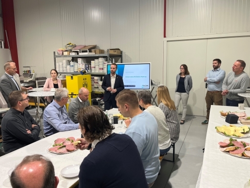 Blick in eine Halle des Unternehmens Logotex; mehrere Menschen sitzen an Tischen, im Hintergrund stehen Bürgermeister Marcel Mittelbach, Dezernentin Jeanette Sebrantke und weitere Personen.