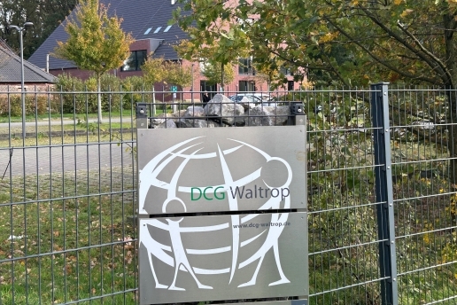 Blick auf das Gelände und die Gebäude der DCG - Die Christliche Gemeinde in Waltrop, im Vordergrund ein Zaun mit einem Schild der DCG.