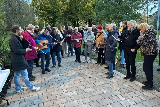Mehrere Menschen stehen im Halbrund im Stutenteichpark Waltrop und halten Liedzettel in den Händen.