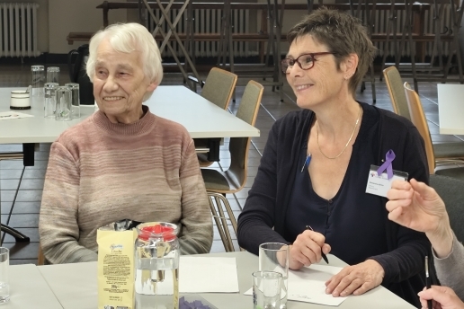 Zwei Frauen sitzen an einem Tisch, vor sich Gläser, eine Getränkekaraffe und einige Blätter.
