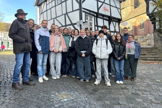 Eine Gruppe steht an der Rösterstraße in Waltrop rund um die Stolpersteine im Boden, im Hintergrund ein Fachwerkhaus und ein Teil der Kirche St. Peter. 