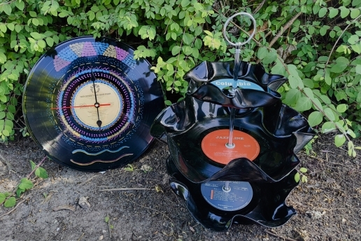 Zwei kreative Objekte aus Schallplatten stehen auf dem Boden, im Hintergrund Heckengrün. 