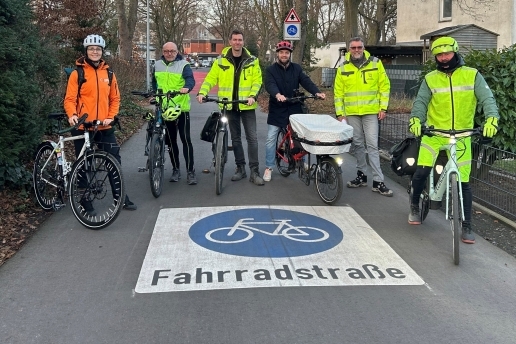 Sechs Personen stehen mit Fahrrädern rund um eine blau-weiße Markierung "Fahrradstraße".  