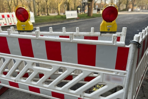 Eine rot-weiße Absperrbake mit Leuchten, im Hintergrund eine Straße. 
