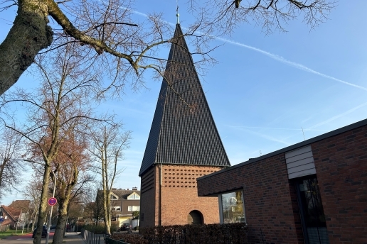 Der Kirchturm von St. Ludgerus, angrenzend die Kita; Bäume.