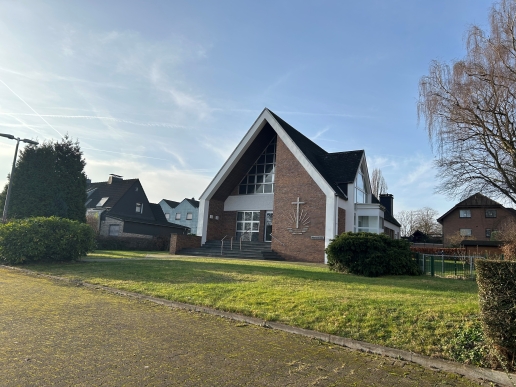 Die Neuapostolische Kirche in Waltrop, im Vorderrund eine Grünfläche, angrenzend Bebauung und Bäume sowie Sträucher. 