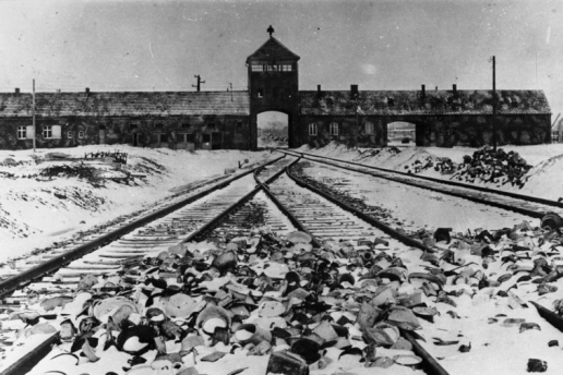 Blick auf das Gebäude der Gedenkstätte von Auschwitz-Birkenau, im Vordergrund Bahngleise.