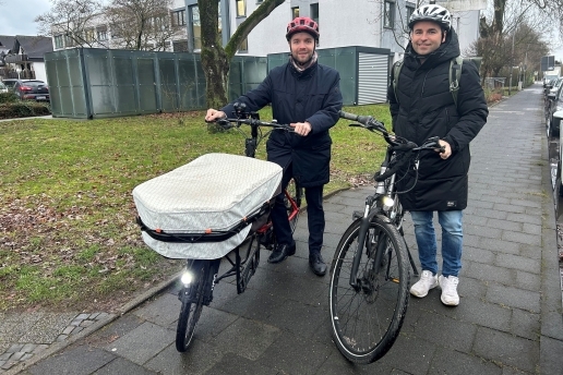 Bürgermeister Marcel Mittelbach und Frank Adamski stehen mit Fahrrädern an der Münsterstraße, i Hintergrund der Fahrradschuppen am Rathaus.