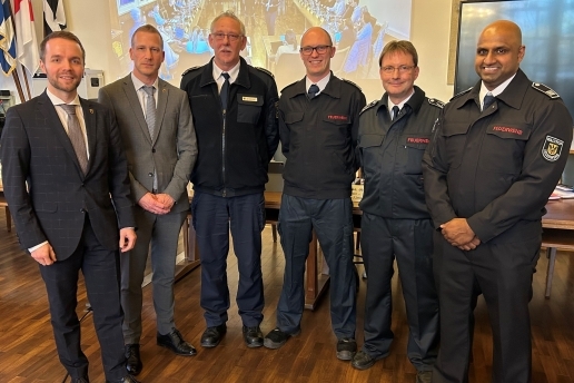 Eine Gruppe von Herren steht im Ratssaal, vier von ihnen in Feuerwehr-Kleidung.