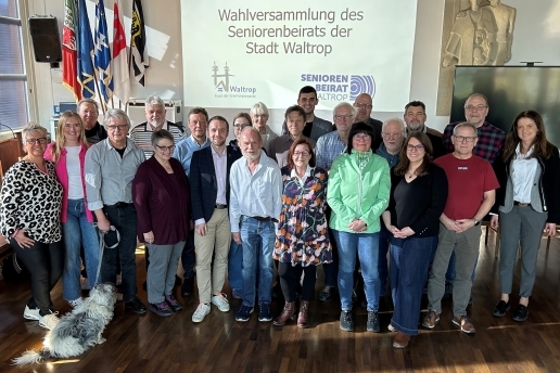 Eine Gruppe Menschen - der Seniorenbeirat Waltrop samt Wahlvorstand - steht im Ratssaal, im Hintergrund eine Beamer-Darstellung an der Wand "Wahlversammlung des Seniorenbeirats der Stadt Waltrop".  