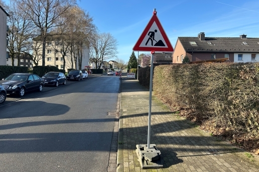 Baustellenschild an der Straße Krusenhof, im Hintergrund die Straße, parkende Autos, Bäume, Häuser, Gehweg. 