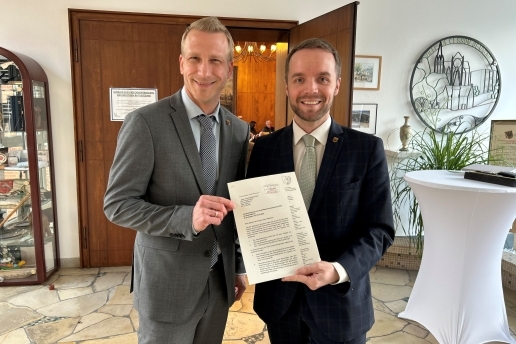 Zwei Männer stehen mit einem Papier vor der Eingangstür in den Ratssaal. 