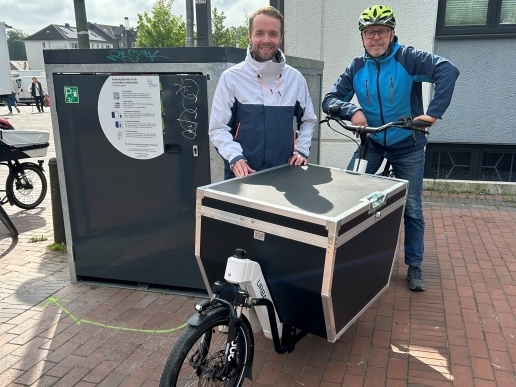 Zwei Personen stehen hinter einem Lastenrad neben einer Fahrradgarage.