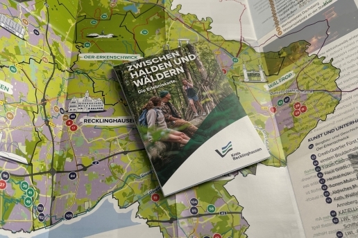 Die Erlebniskarte "Zwischen Halden und Wäldern" liegt zusammengeklappt auf einer ausgebreiteten Version dieser Karte auf einer Fläche. 