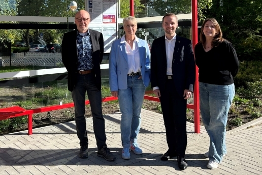 Zwei Männer und zwei Frauen stehen an einer Bushaltestelle.