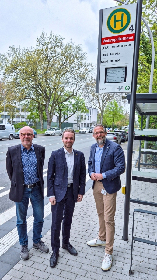 Drei Herren stehen an einer Bushaltestelle. 