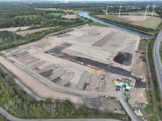 Luftbild des Gewerbegebiets Im Dicken Dören in der Bauphase, im Hintergrund Landschaft, Kanal, Windräder, rechts eine Straße
