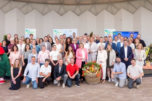 Eine Gruppe steht bei der IGA-Picknick-Pressekonferenz in einem Raum, zwischen den Personen steht ein großer Picknick-Korb.