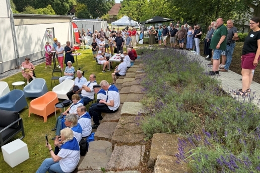 Mehrere Menschen stehen im Lesegarten hinter dem HBBK und schauen auf eine Bühne. 