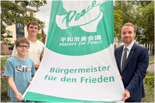 Bürgermeister Marcel Mittelbach hisst am 8. Juli 2026 gemeinsam mit Felix Greßkötter, Tagespraktikant im Bürgermeisterbüro (1. v. l.) und dem Auszubildenden Linus Witte (2. v. l.) die Mayors for Peace-Flagge vor dem Waltroper Rathaus. 