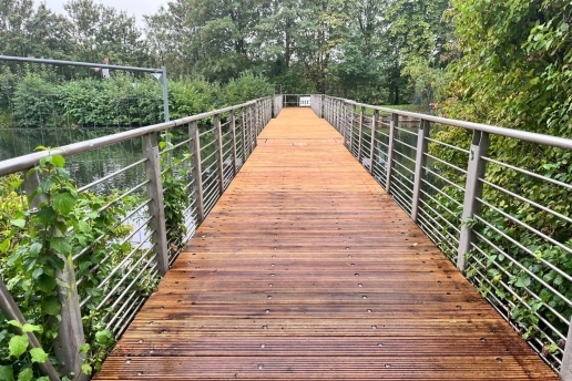 Eine Brücke mit Holzbelag und Metall-Geländer am Kanal. 