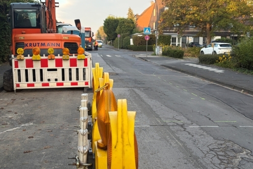 Baustellenzaun, Baufahrzeuge, eine Straße und Bebauung. 
