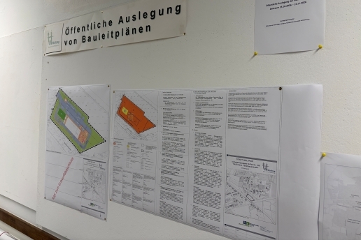 Pläne mit Text hängen an einer Wand, darüber ein Schild "Öffentliche Auslegung von Bauleitplänen".