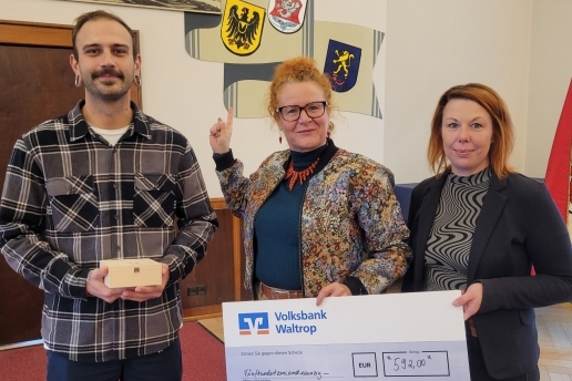 Drei Personen stehen vor drei Wappen, halten eine Holzschachtel und einen Spendenscheck in den Händen.