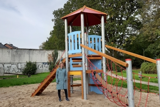 Eine Frau steht vor einem Spielgerät mit Klettergelegenheiten, Rutsche und Turm.