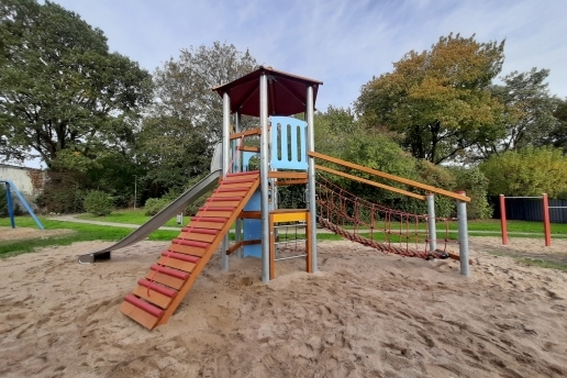Ein Spielgerät mit Klettermöglichkeiten, Rutsche und Turm in einem Sandkasten.