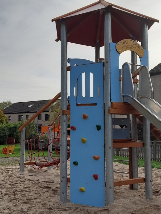 Ein Spielgerät mit Kletterwand, Turm und Rutsche in einem Sandkasten. 