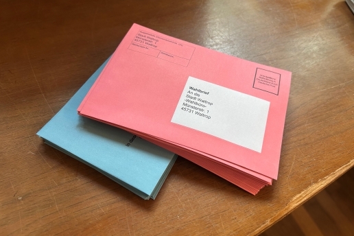 Ein Stapel Wahlbriefe in roten Umschlägen liegt auf einem Tisch.