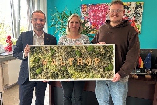 Bürgermeister Marcel Mittelbach (links) steht mit Stefanie Miller und Maurits Müller von der DRK-Kita an der Hafenstraße im Büro des Bürgermeisters und halten ein Bild mit Waltrop-Schriftzug in der Hand.