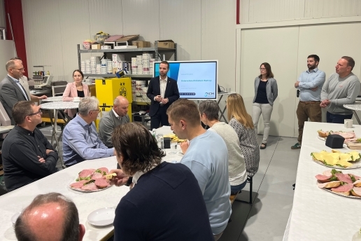 Blick in eine Halle des Unternehmens Logotex; mehrere Menschen sitzen an Tischen, im Hintergrund stehen Bürgermeister Marcel Mittelbach, Dezernentin Jeanette Sebrantke und weitere Personen.