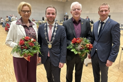 Vier Personen, zwei davon halten Blumensträuße in der Hand, stehen in der Stadthalle. 