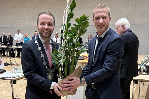 Zwei Personen stehen in der Stadthalle; sie halten eine Topfpflanze.