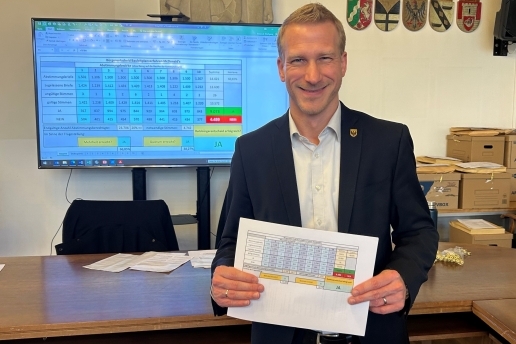 Stefan Wilke hält vor einem Monitor den Zettel mit den Ergebnissen des Ratsbürgerentscheids in die Kamera.