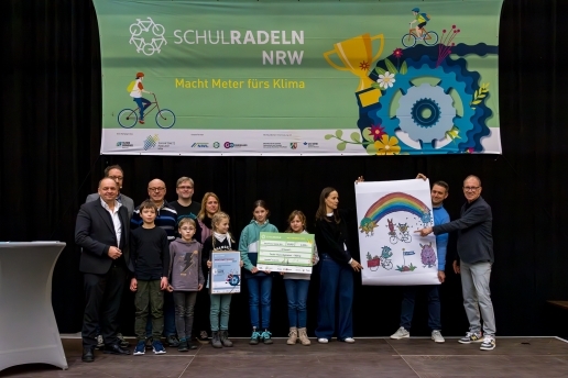 13 Personen - Kinder und Erwachsene - stehen vor einem Banner "Schulradeln NRW", einige halten Plakate in der Hand.