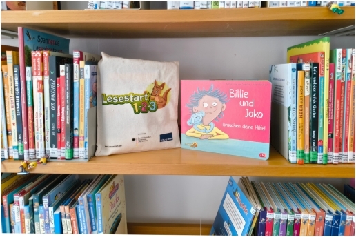 Bücherregal im Kulturwohnzimmer des Dritten Orts mit Werbung für die Aktion %22Lesestart 1-2-3%22