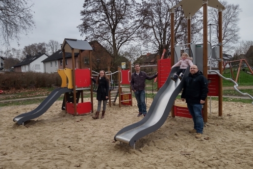 Rund um ein Spielgerät auf einem Spielplatz stehen drei Erwachsene und ein Kind. 