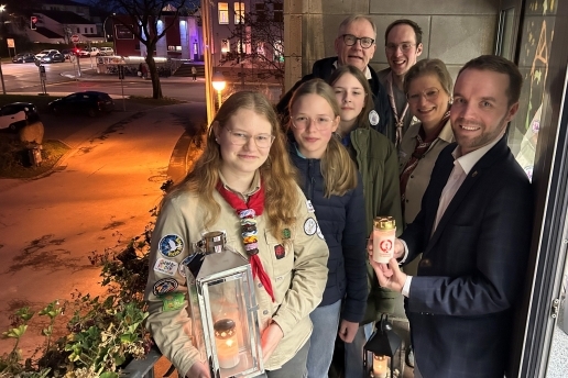 Auf dem Rathaus-Balkon stehen sieben Personen, die Kerzen und Windlichter in den Händen halten.
