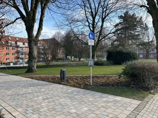 Blick in den Stutenteichpark mit Rasenflächen, befestigten Wegen, Sitzgelegenheiten, Bäumen, Beeten; im Hintergrund Bebauung. 