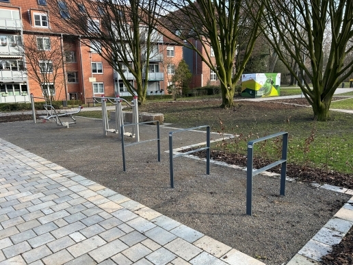 Sportgeräte im Stutenteichpark, im Hintergrund Rasenflächen und das Hirschkamp-Seniorenzentrum sowie ein mit Graffiti versehenes Trafo-Haus. 