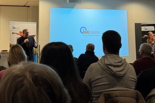 Auftaktveranstaltung Macherstadt im Foyer der Stadthalle Waltrop, im Vordergrund sitzen Personen in Stuhlreihen, im Hintergrund redet eine Person, an der Wand eine Präsentation der IKK classic.
