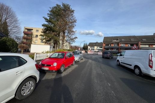 Blick in die Kettelerstraße, links und rechts parken Autos, im Hintergrund Bäume und Gebäude und rot-weiße Absperrungen für eine Baustelle. 