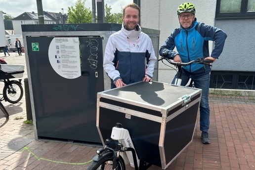 Zwei Personen stehen hinter einem Lastenrad neben einer Fahrradgarage.